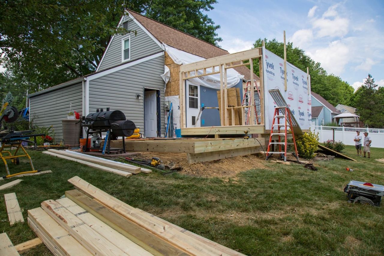 A house under construction, with wooden framing and a deck, on a grassy lawn.
